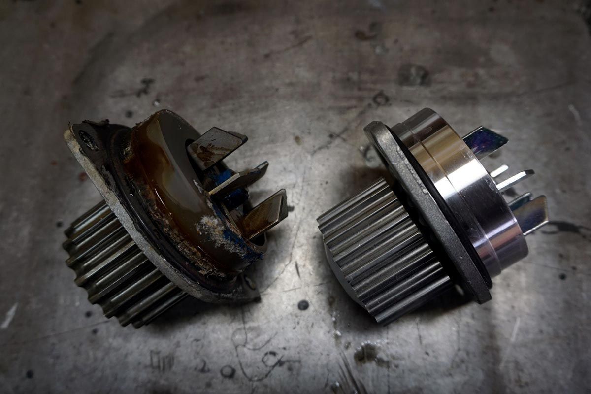 Two water pump assemblies, one damaged and corroded, on a metal surface.